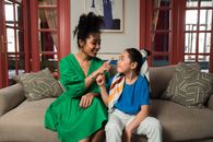 Woman in Green Dress Sitting on Couch Beside Woman in White and Black Stripe Shirt