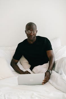African American man wearing glasses working remotely on a laptop at home.