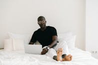 Man in Black Crew Neck T-shirt and White Pants Sitting on Bed