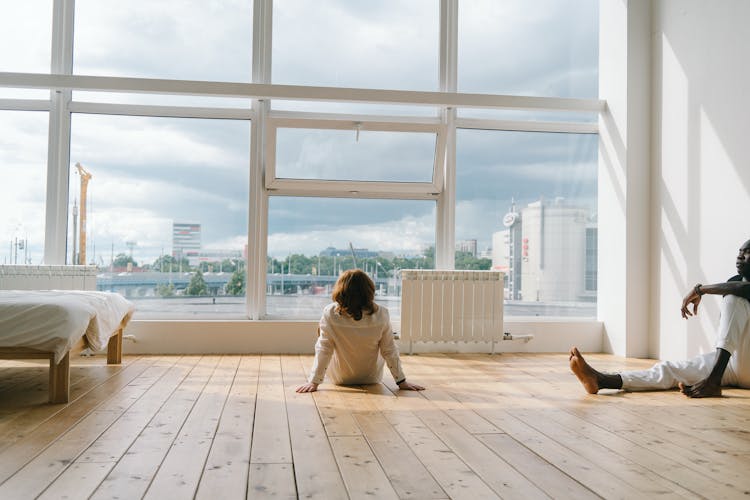 Man And Boy Sitting On Floor Of Room With Large Windows