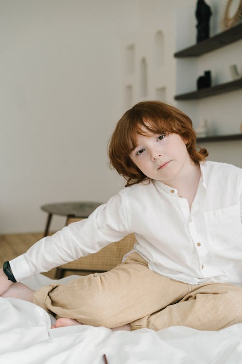A Young Boy in White Long Sleeves Sitting on the Bed