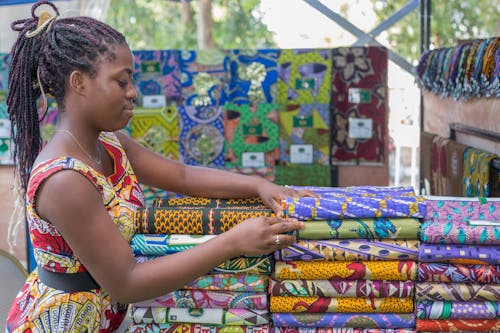 Young Woman Standing next to Piles of Colorful, Patterned Fabric 
