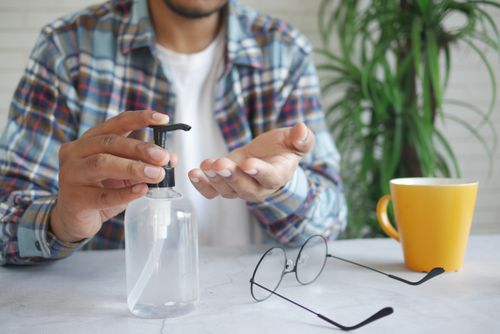 Free A man in a plaid shirt applies hand sanitizer indoors, promoting cleanliness and hygiene. Stock Photo