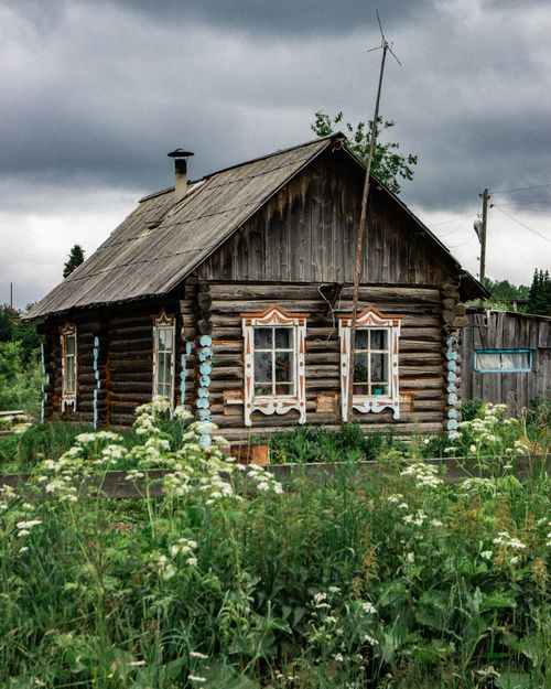Free A rustic wooden cabin surrounded by lush greenery and wildflowers under stormy skies. Stock Photo