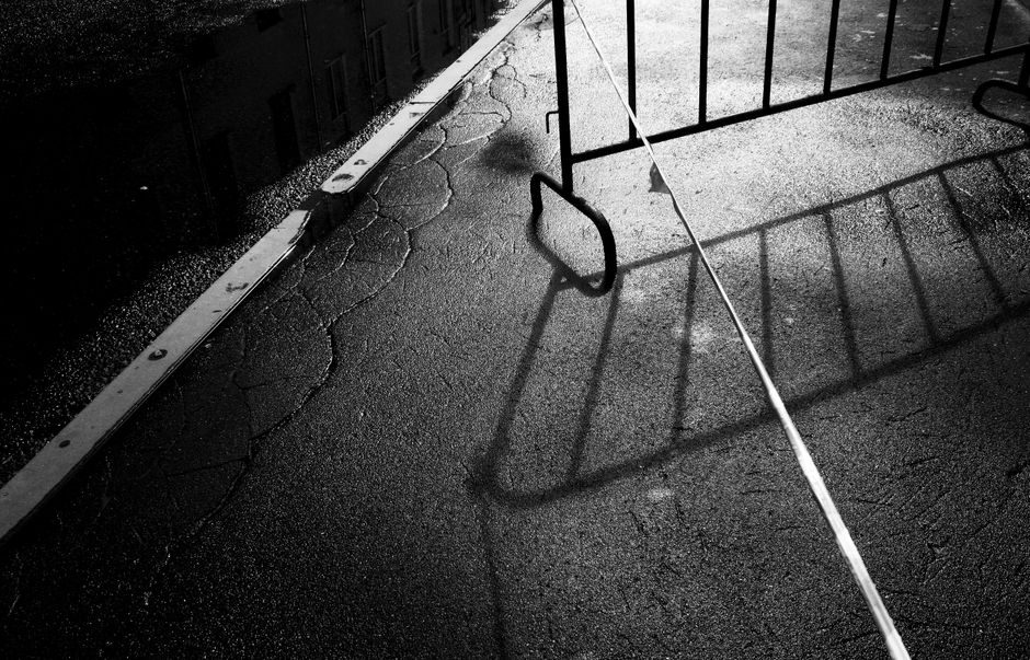 Moody black and white photo featuring cracked pavement with a barrier casting shadow.