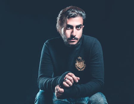 一名时尚男子留着胡须、穿着毛衣，在黑暗的工作室里严肃地摆姿势