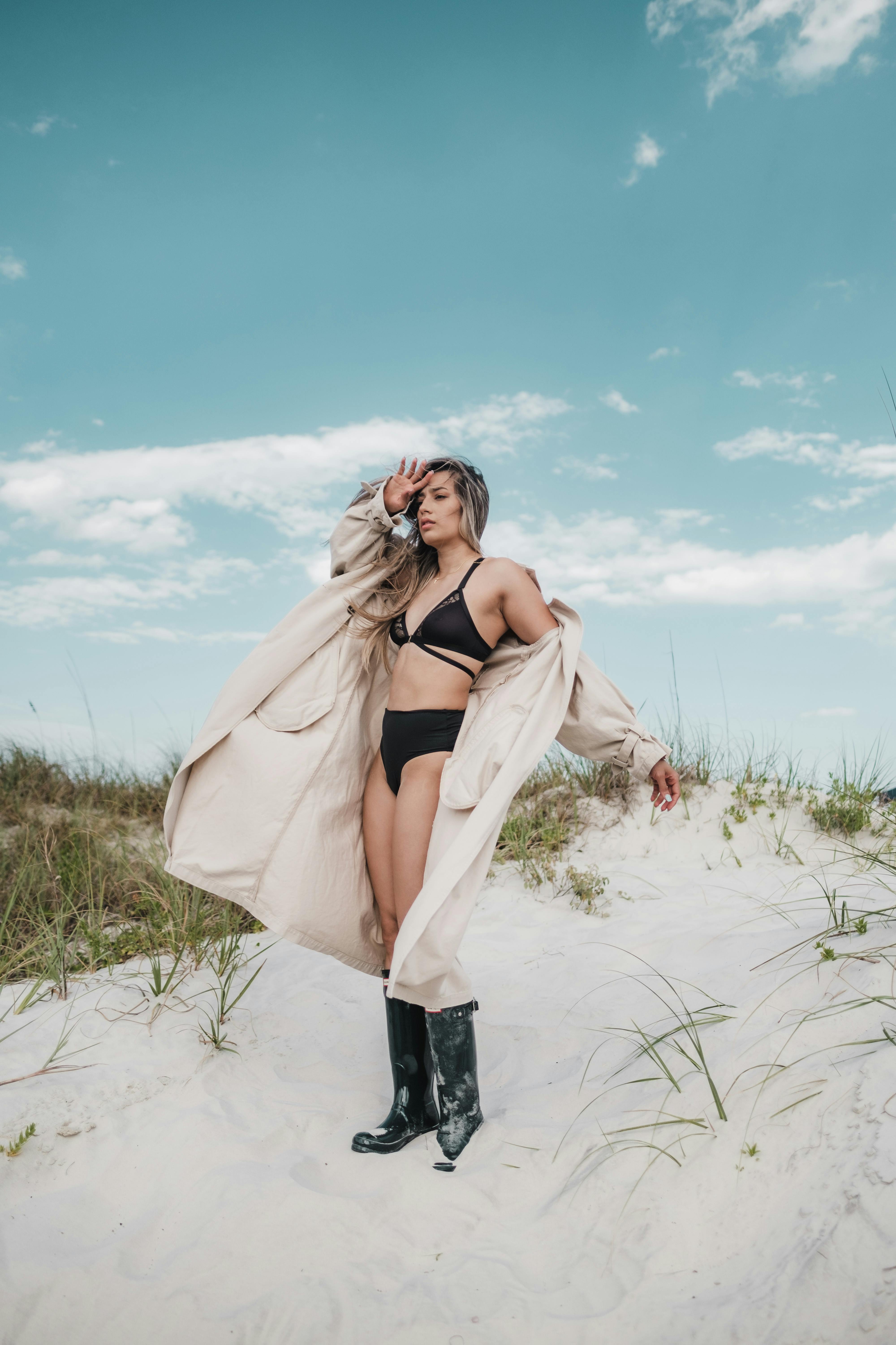 Woman in a bikini and coat standing on a sunny beach with a clear blue sky.
