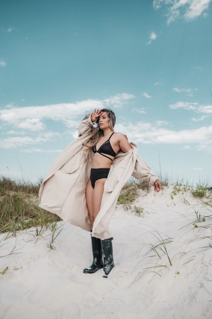 Woman in a bikini and coat standing on a sunny beach with a clear blue sky.