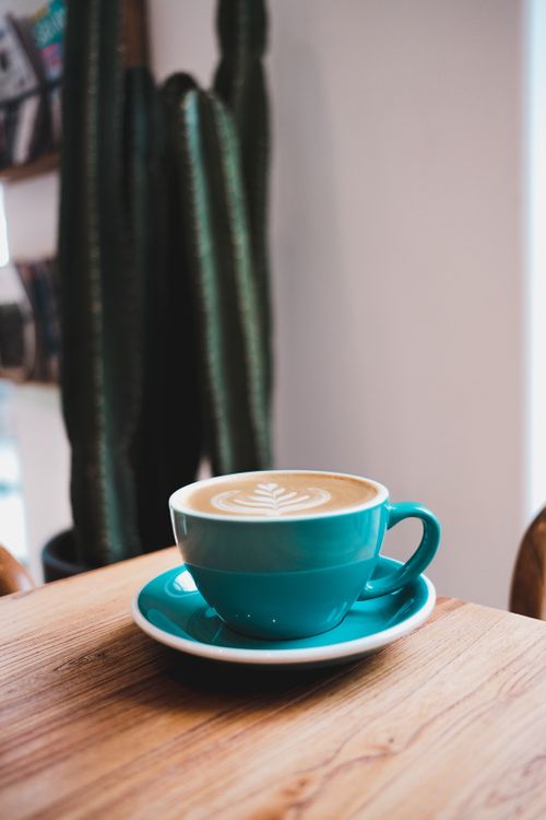 Free A beautiful cappuccino with latte art in a turquoise cup, set in a cozy indoor cafe environment. Stock Photo