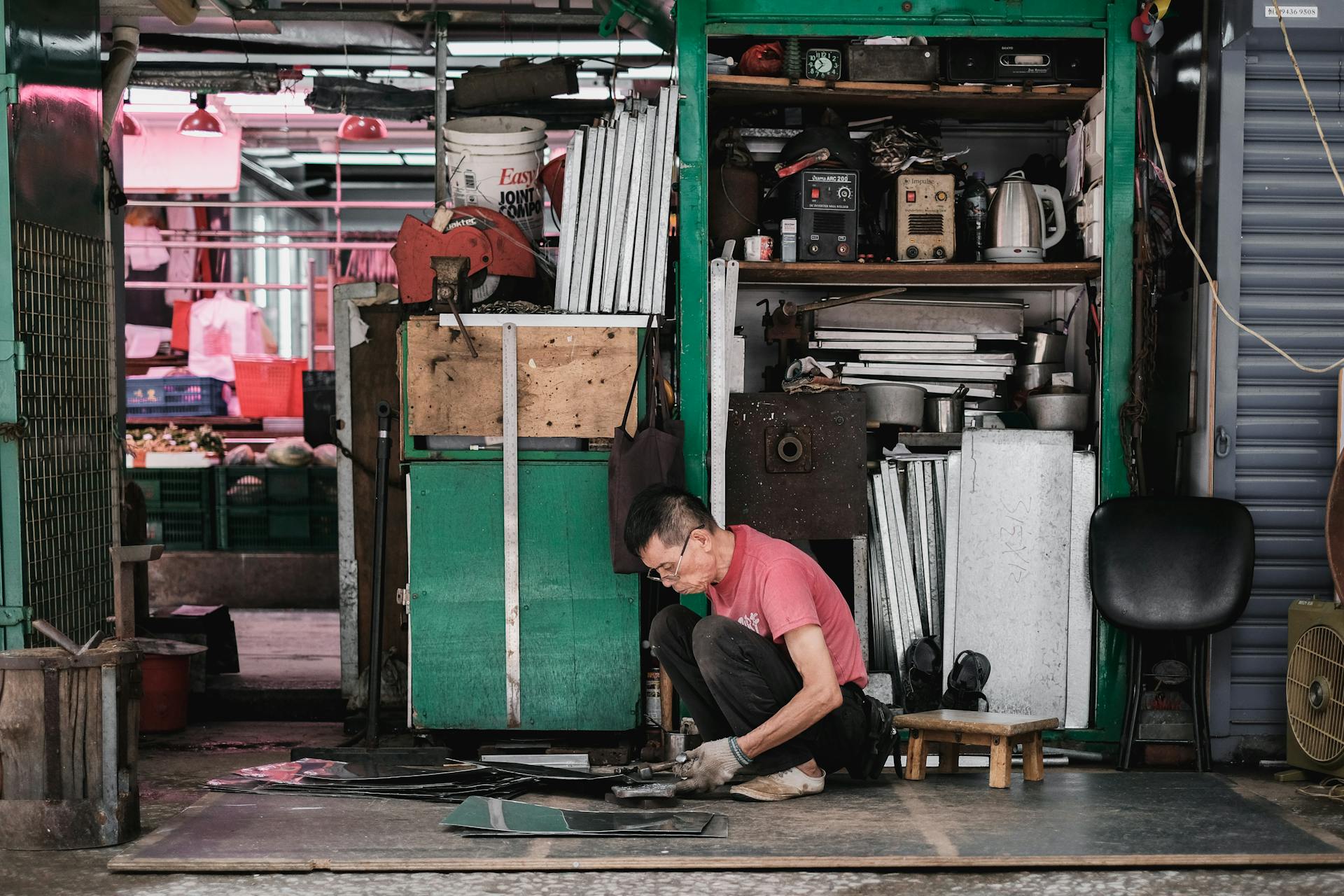 Man engaged in metalwork in a traditional Hong Kong street stall, showcasing craftsmanship.