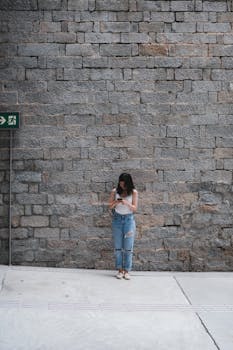 Woman in ripped jeans texting on phone against a stone wall in Hong Kong.