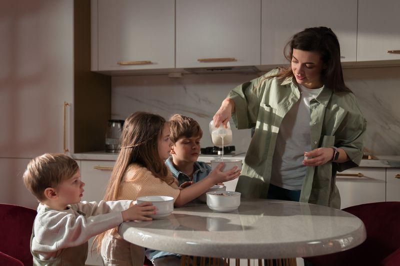 A mother pours milk into bowls for her three children during breakfast time at home.