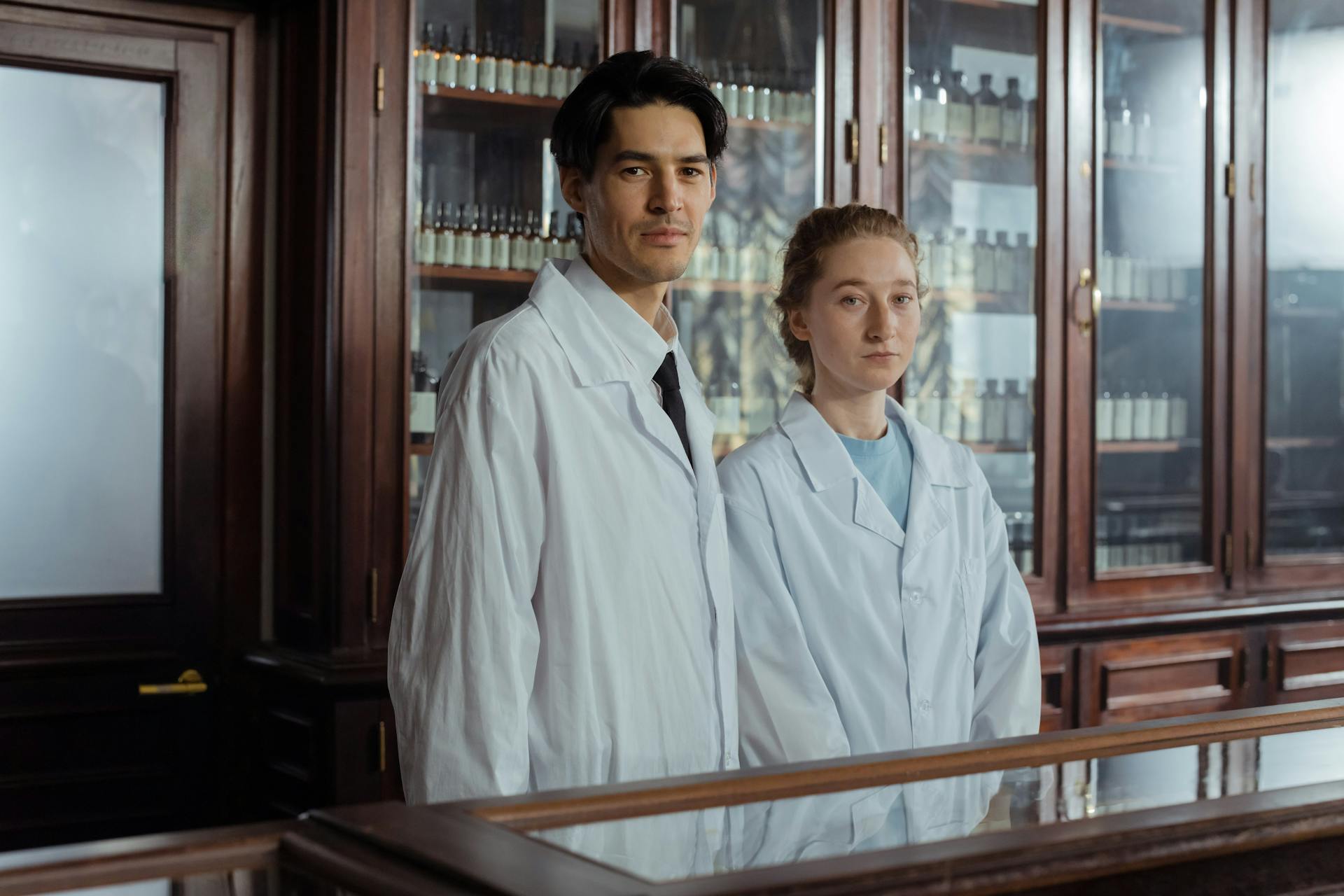 Man and Woman in White Gowns Standing behind the Counter in a Vintage Pharmacy