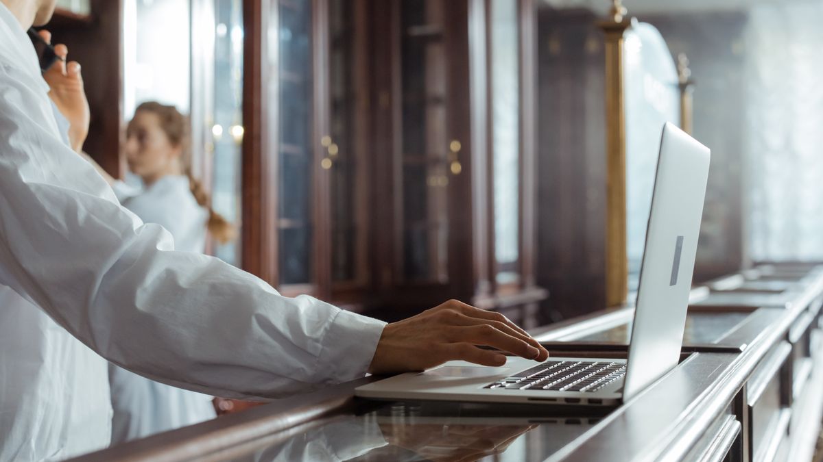 Person in a white coat using a laptop in a laboratory.