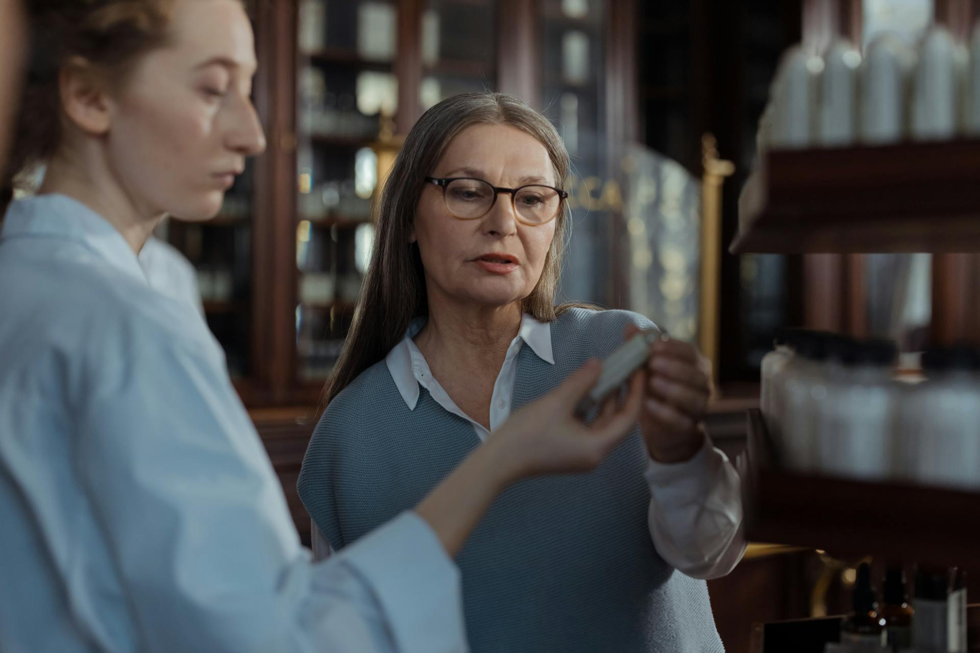 An elderly woman discussing medication options with a pharmacist at a pharmacy counter.