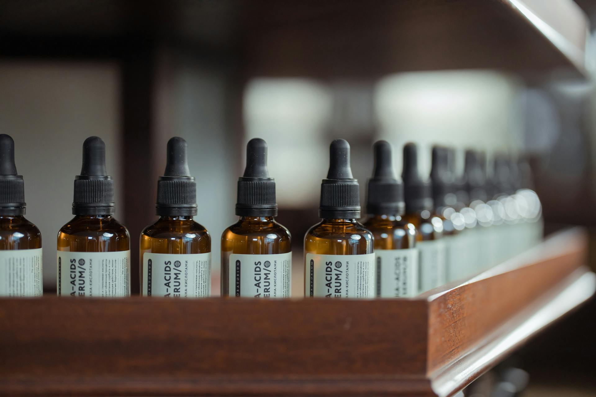 Row of brown serum bottles with dropper caps aligned on a wooden shelf.