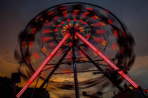 Free A ferris wheel spins in colorful lights at dusk, creating a dynamic motion blur effect against the night sky. Stock Photo