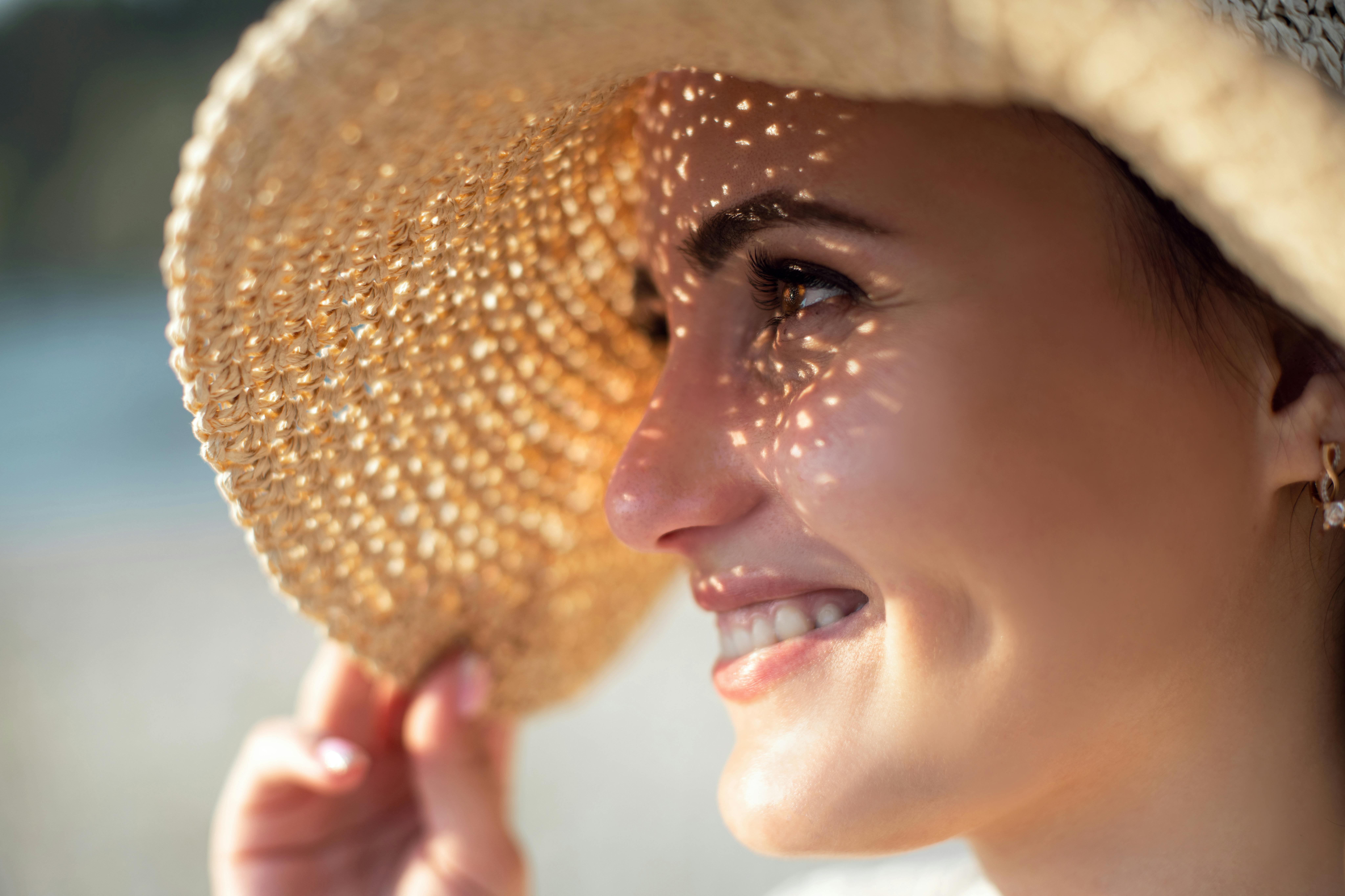 Close-up portrait of a smiling woman in a sun hat, embracing the sunlight outdoors.
