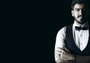 一位时尚男子戴着领结和背心，在黑暗背景下自信地摆出姿势