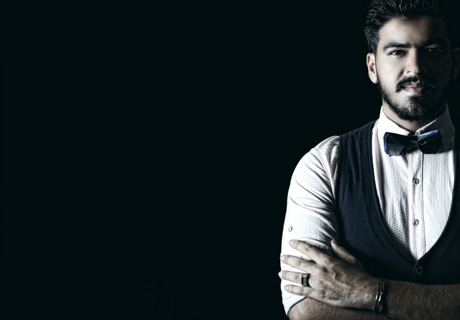 A stylish man wearing a bow tie and vest, posing confidently against a dark background. A stylish man wearing a bow tie and vest, posing confidently against a dark background.