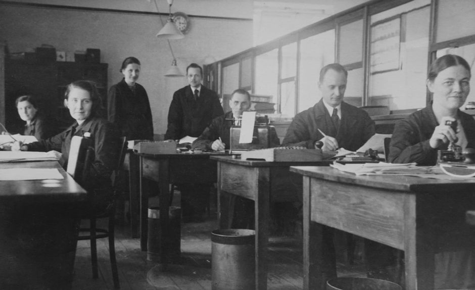 Retro black and white photo of office workers at desks, exuding a vintage workplace atmosphere.