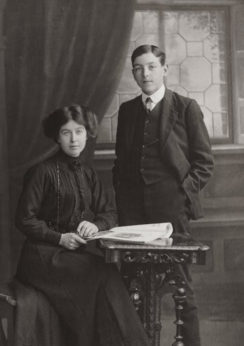 A Gentleman Standing Beside A Woman Seated By The Table