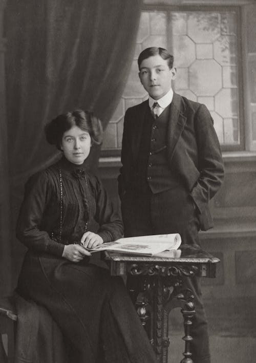 A Gentleman Standing Beside A Woman Seated By The Table