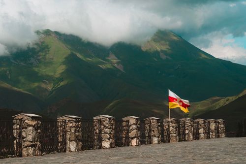 Free Scenic view of lush mountains with a colorful flag and stone fence in North Ossetia, Russia. Stock Photo