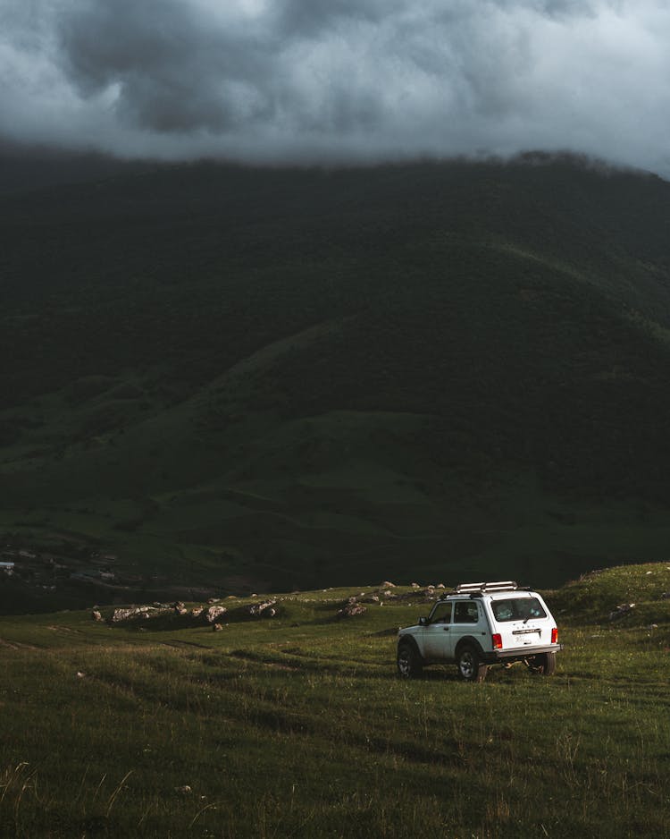 White SUV Parked On Green Grass Field Near Mountain