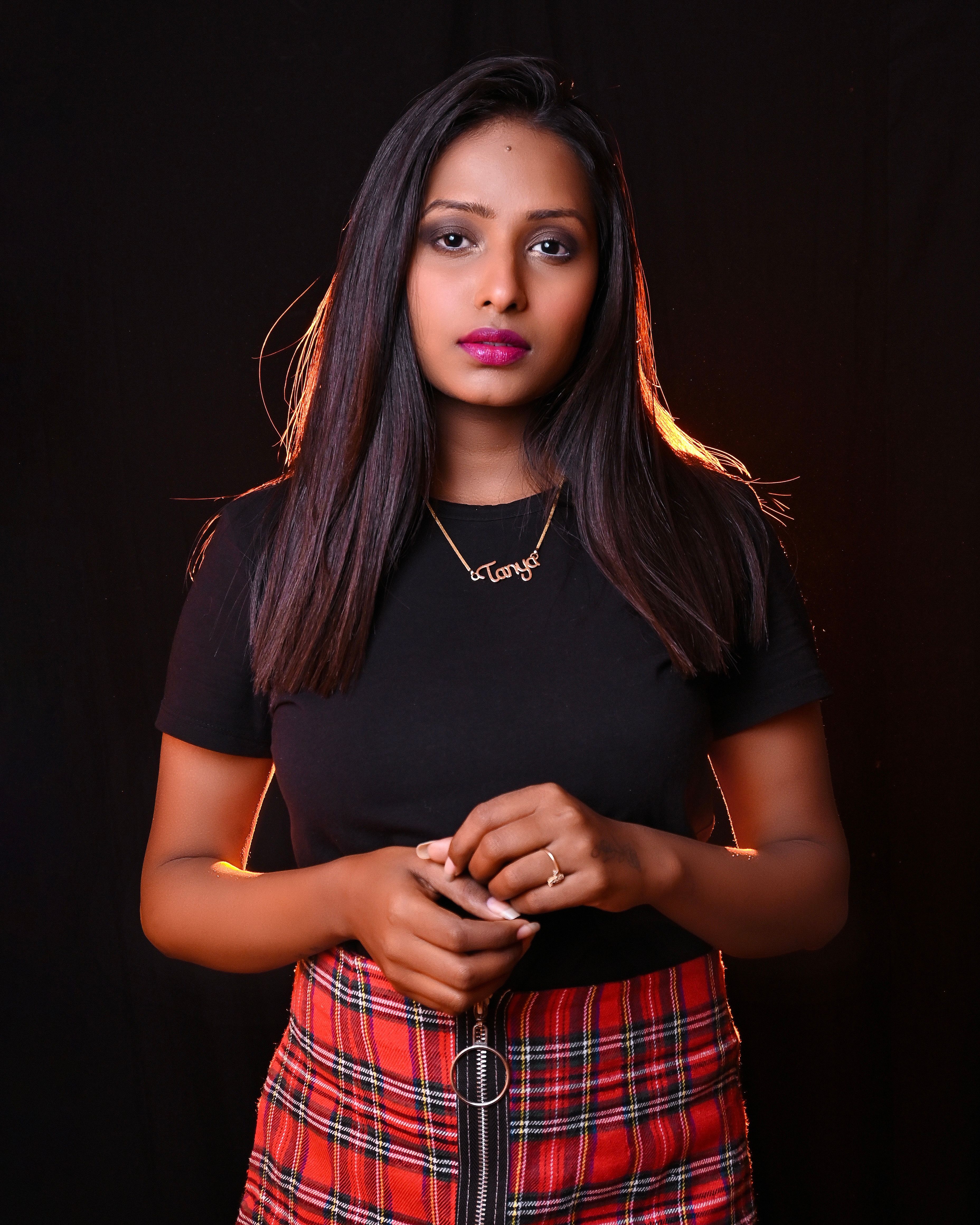 Studio portrait featuring a woman in a plaid skirt and black top, set against a dark backdrop.