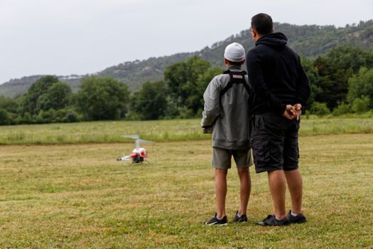 Father and son bonding while flying a radio-controlled helicopter in an open field.