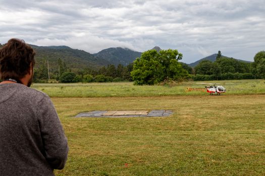 Man enjoying leisure time with a model helicopter in a picturesque field with hills in the background.