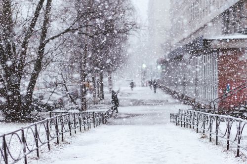 Free A tranquil urban scene with heavy snowfall. Bare trees and blurred figures add depth to the winter atmosphere. Stock Photo