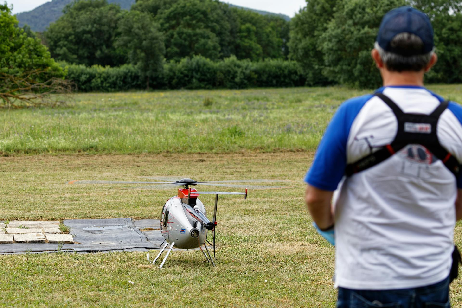 Man controlling a remote-controlled helicopter outdoors in a grassy field.