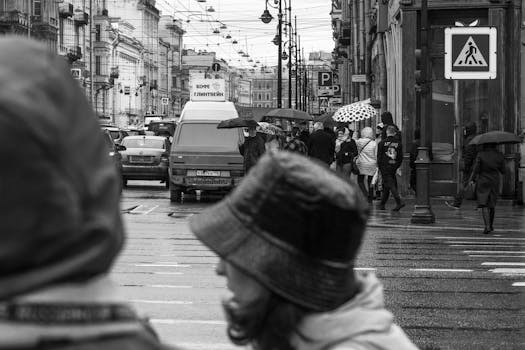 Black and white photo capturing a bustling city intersection on a rainy day.