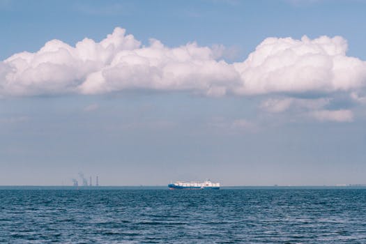 A distant cargo ship sails under a vast sky filled with dramatic clouds over a calm sea.