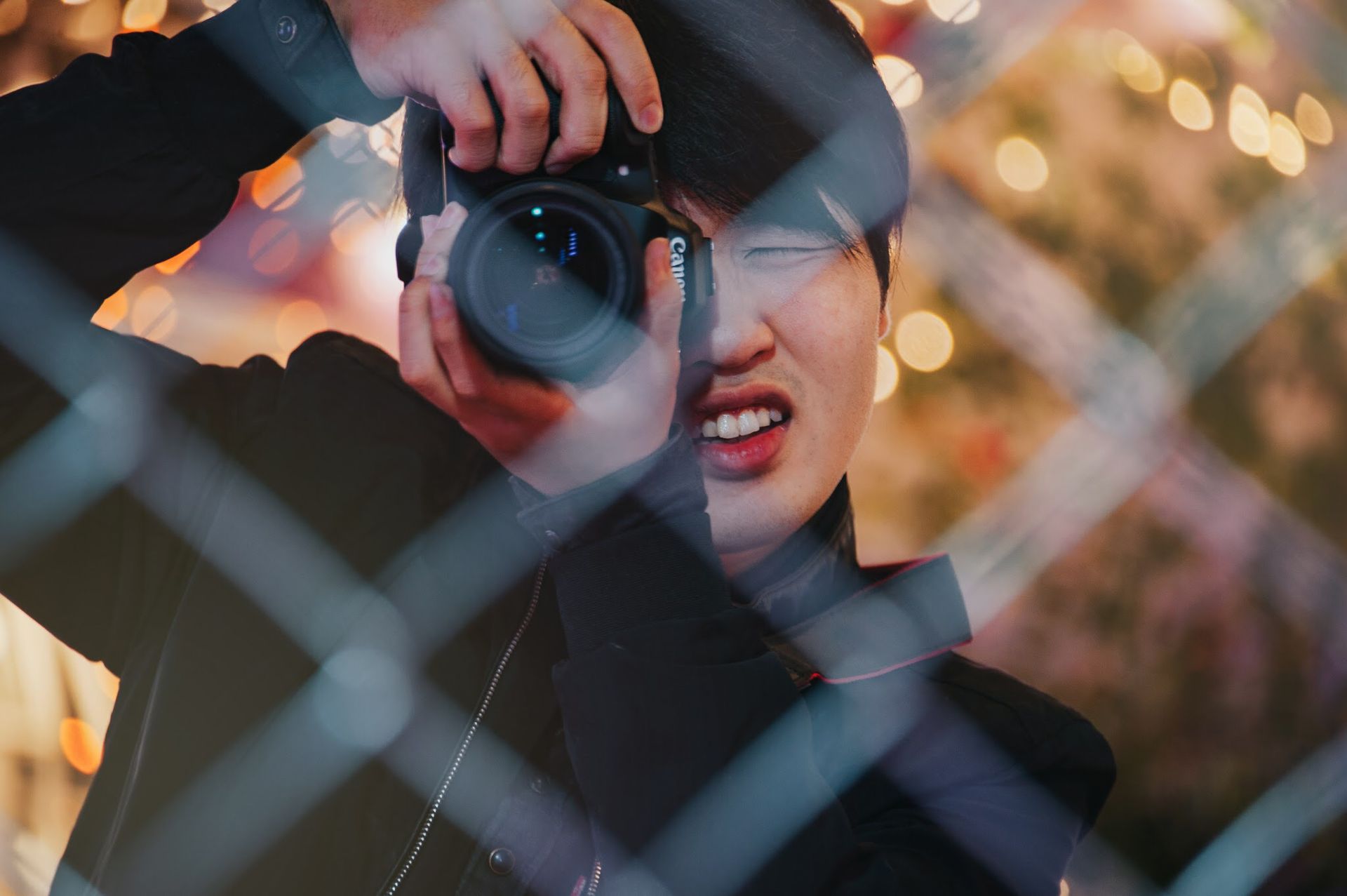 Young man taking a photograph through wire mesh with a camera.