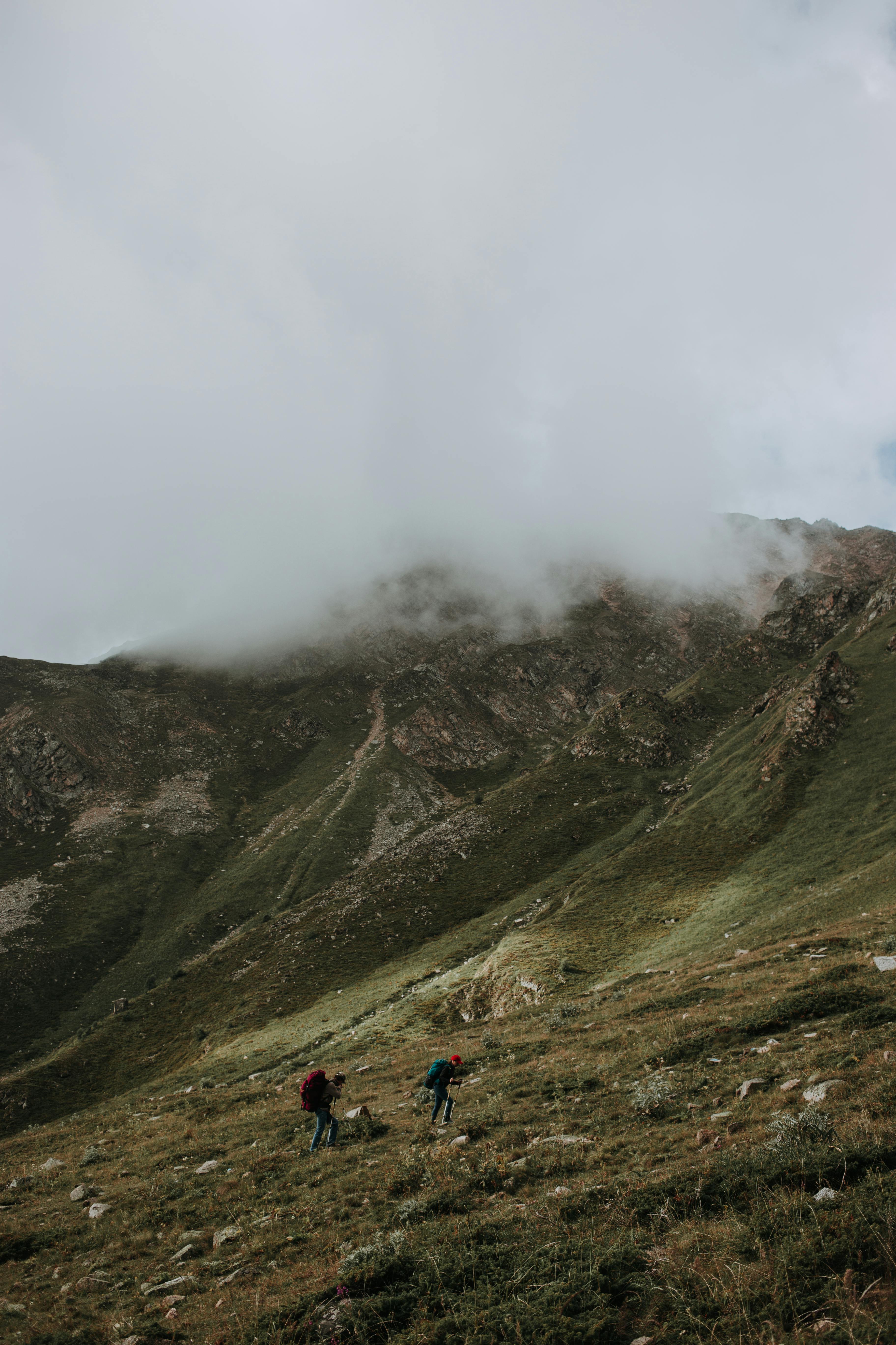 Two hikers traverse a grassy mountain under clouds in North Ossetia, Russia.