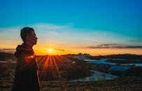 一名男子站在宁静的自然景观中，映衬着充满活力的日落