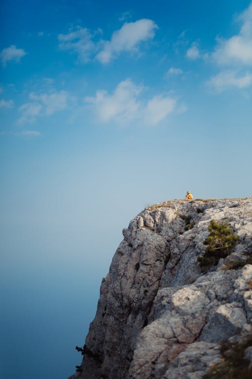 Free Person in Yellow Shirt Sitting on Gray Rock Formation Under Blue Sky Stock Photo
