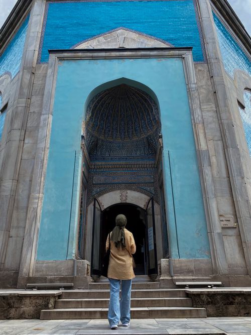 Free A woman stands at the entrance of a historic blue-tiled tomb, showcasing its intricate architecture. Stock Photo