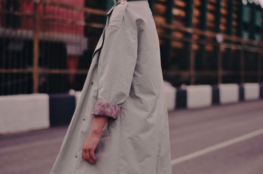 Close-up of a person wearing a stylish coat in an urban environment with a blurred background.