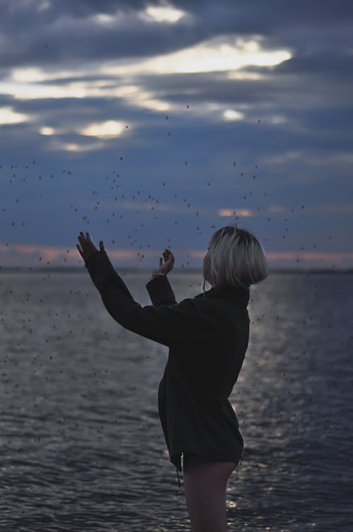 Woman in Black Jacket Standing near the Body of Water 