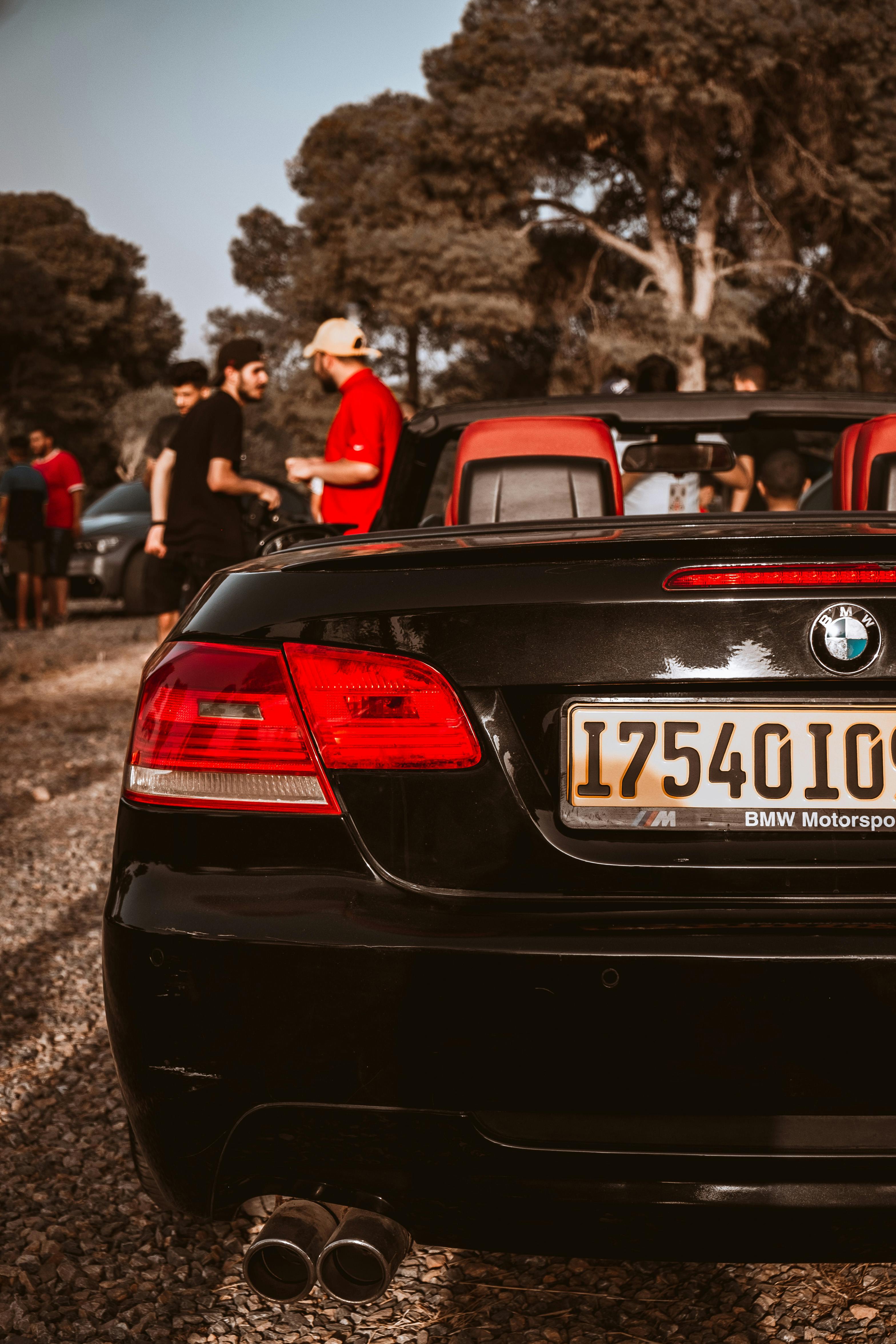 Rear view of a luxury BMW convertible with people gathered outdoors on a sunny day.