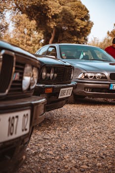 Close-up of classic and modern cars parked outdoors on a gravel area during daytime.