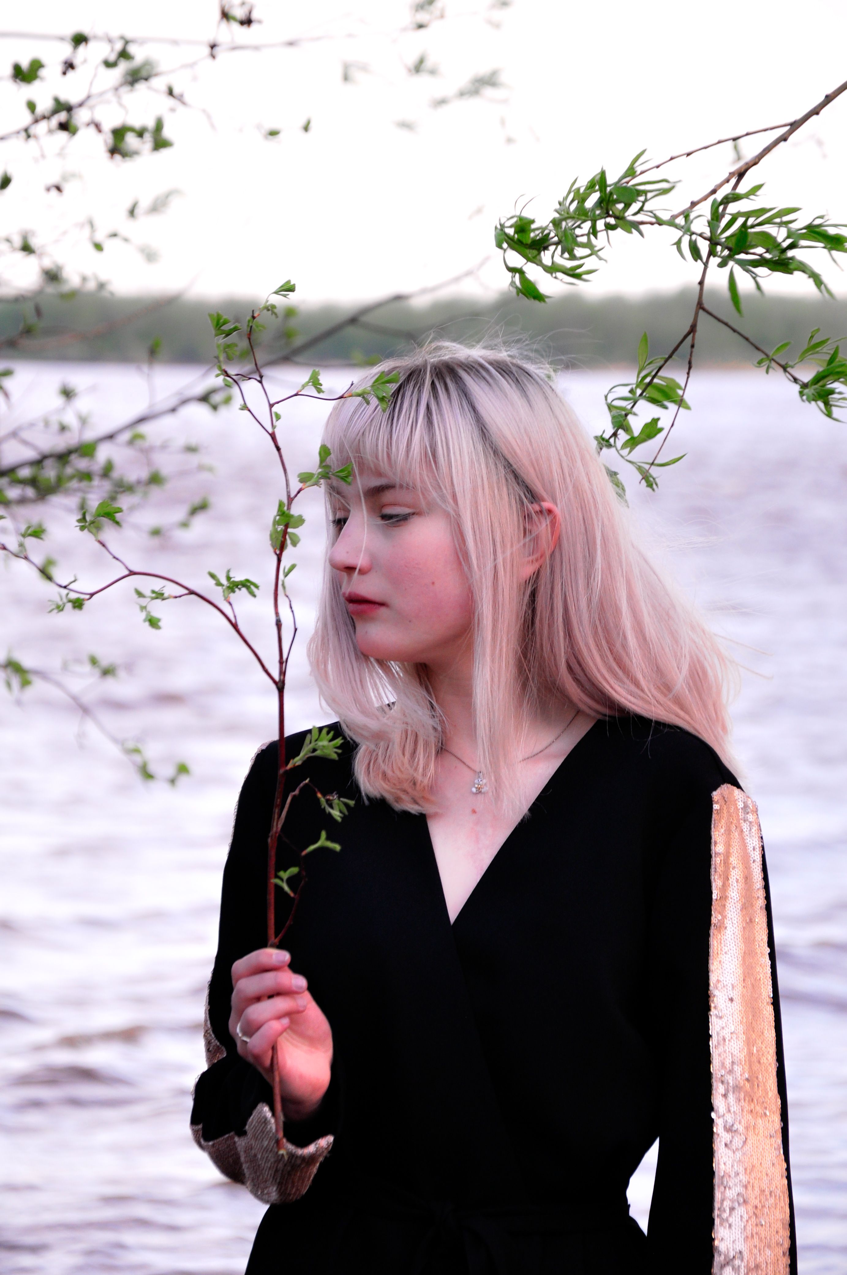 Portrait of a woman holding a twig by the water, surrounded by nature.