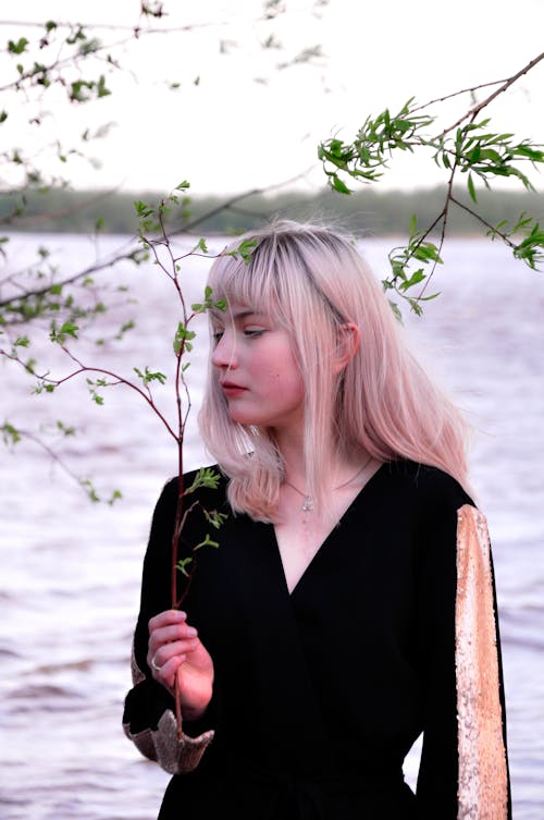 Photo of a Woman in a Black Top Holding a Twig with Green Leaves