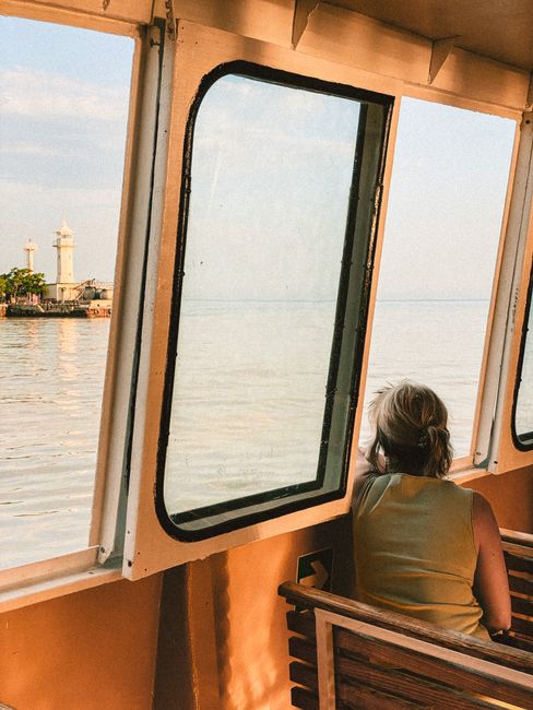 Woman sitting on a ferry gazing out at the sea and lighthouse, captured in sunset hues.