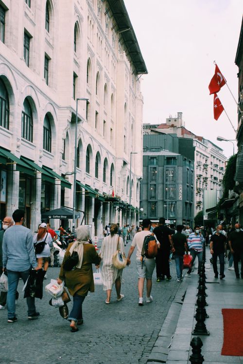Free A lively street with people walking by historic architecture and city flags waving. Stock Photo