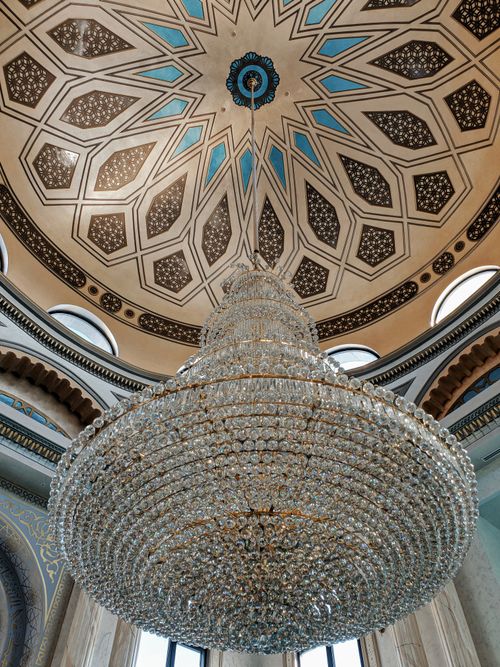 Free Opulent chandelier set against a beautifully ornate cathedral dome, showcasing intricate patterns and architectural elegance. Stock Photo
